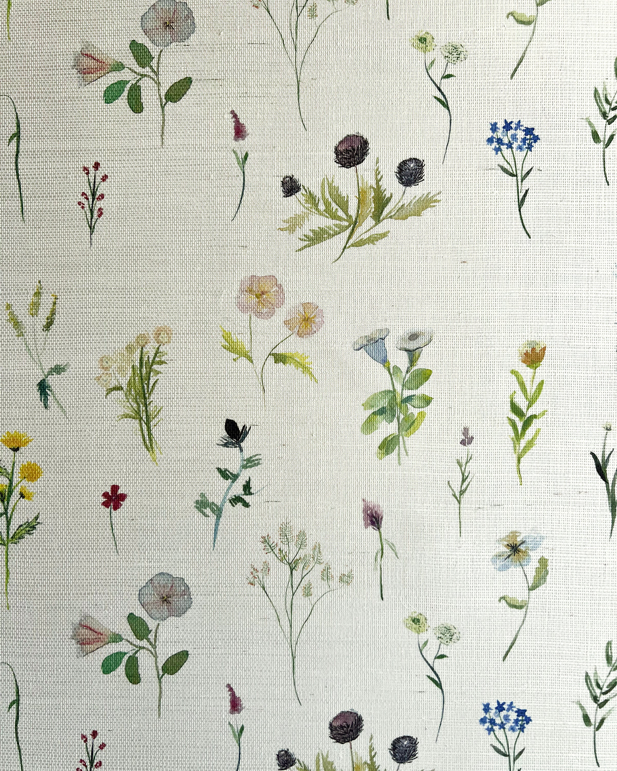 Detail of fabric in a painterly flower print in green and pastels on a cream field.