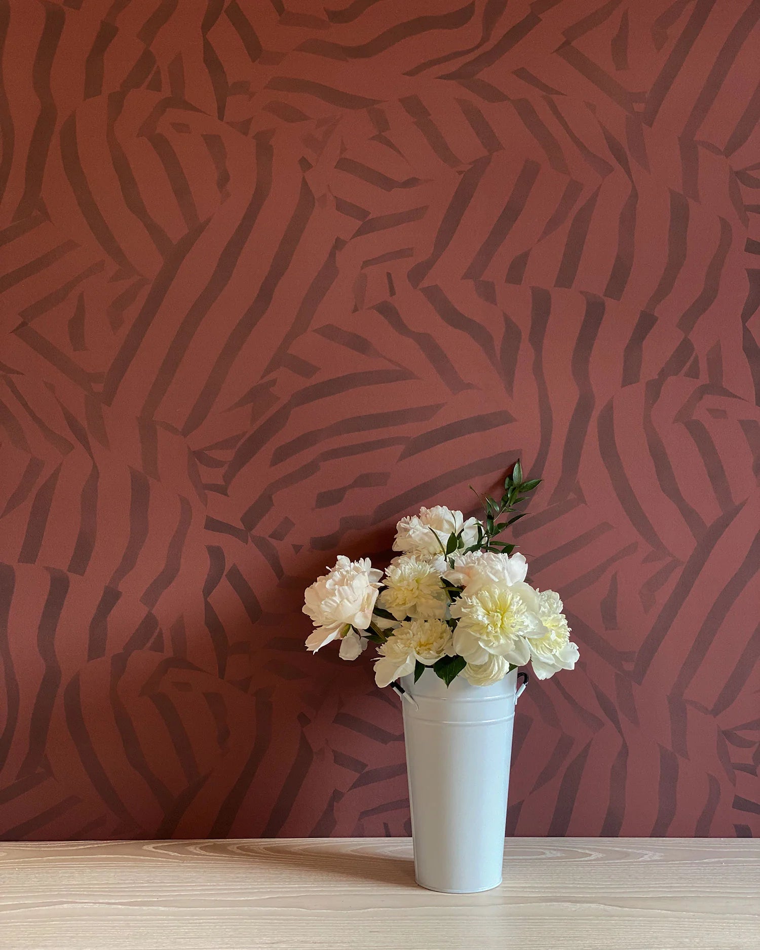 A vase of flowers stands in front of a wall papered in a playful broken stripe print in purple on a red field.