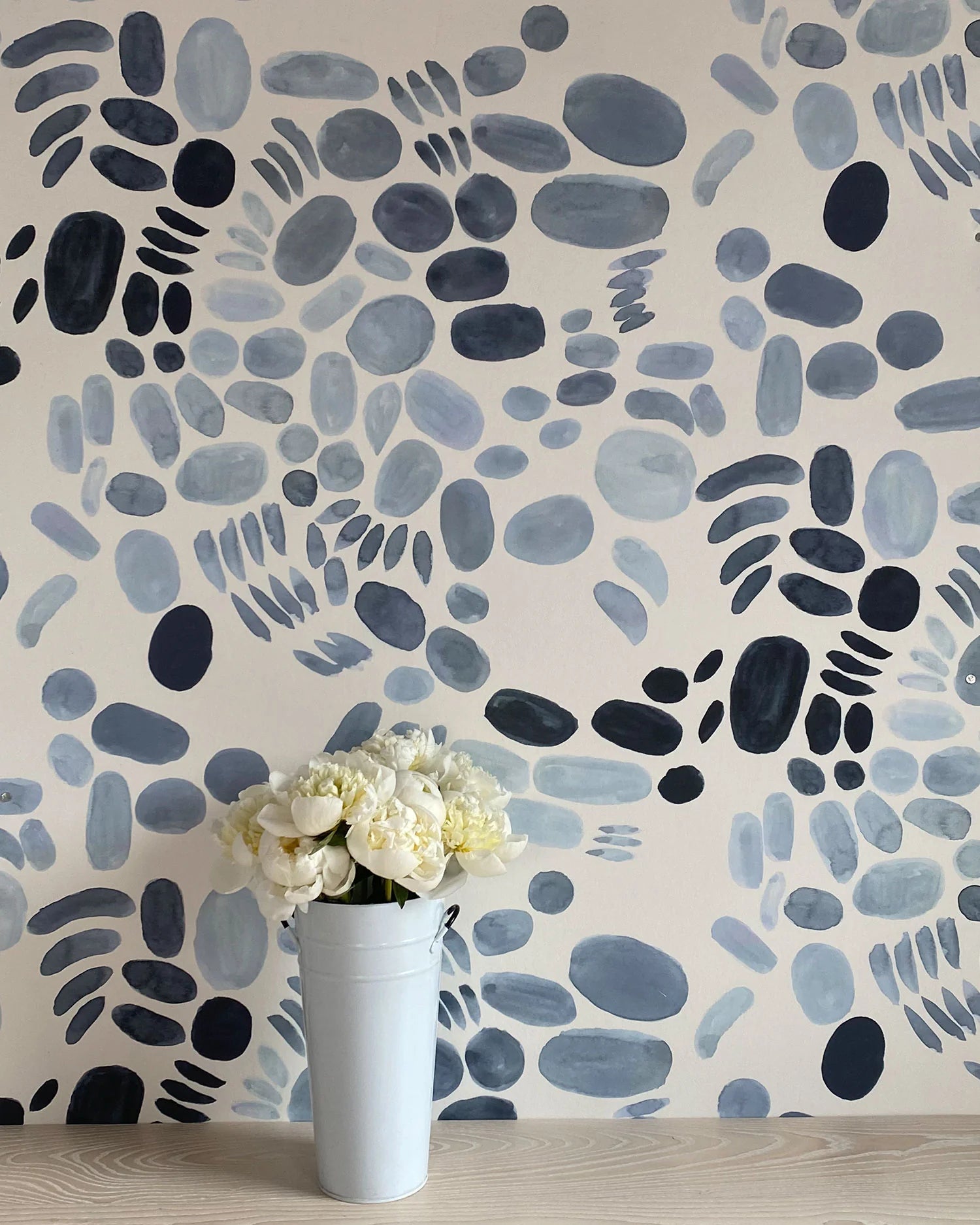 A vase of flowers stands in front of a wall covered in a playful paint blotch print in blue and gray on a cream field.