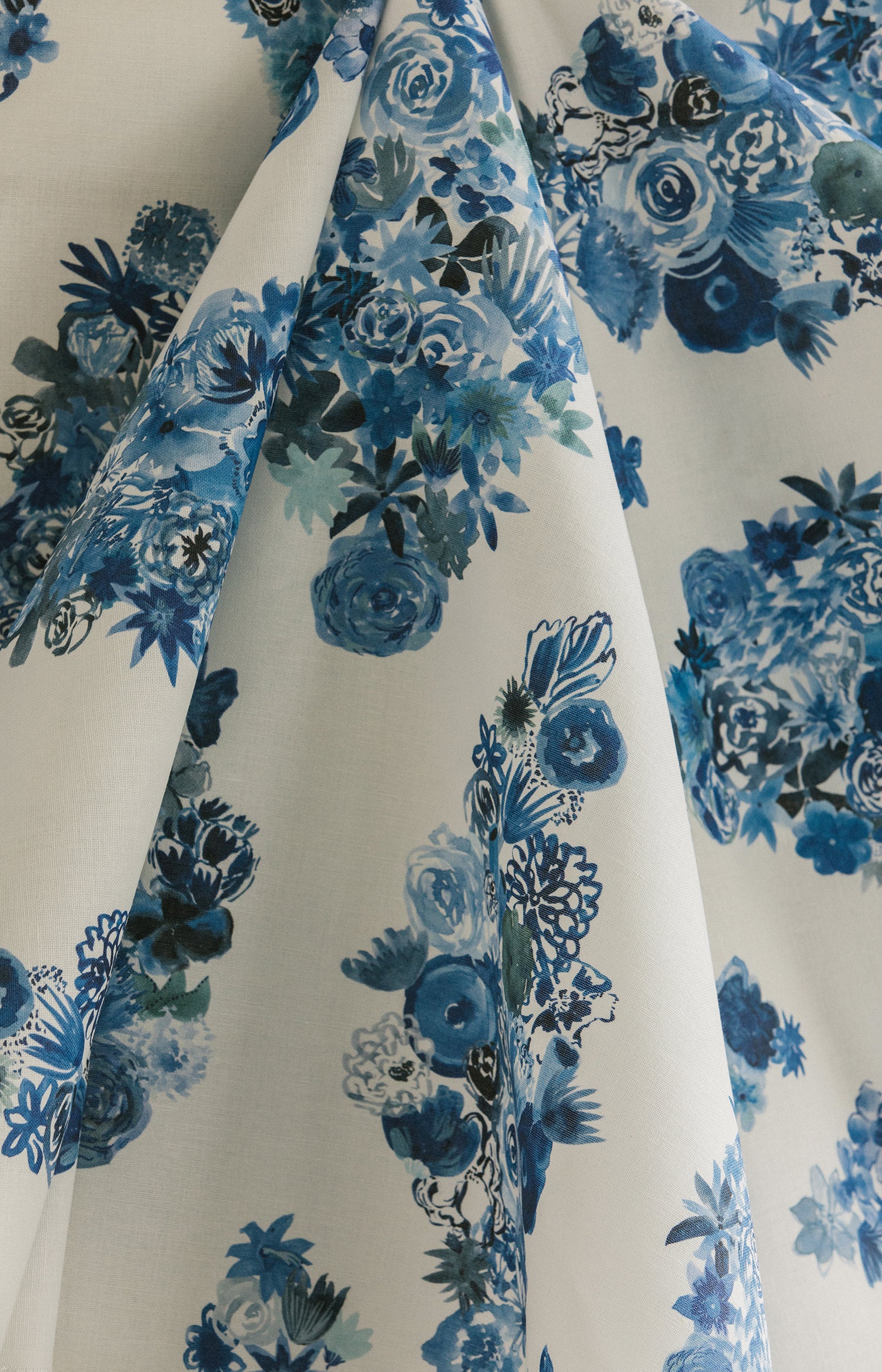 Draped fabric yardage in a painterly floral print in shades of blue and navy on a cream field.