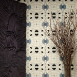 Flowers and a black room divider stand in front of a wall papered in a watercolor ink blot print in charcoal, black and tan.