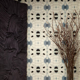 Flowers and a black room divider stand in front of a wall papered in a watercolor ink blot print in charcoal, black and tan.