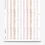 Partially unrolled wallpaper yardage in a painterly stripe print in shades of pink, gray and cream on a white field.
