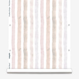 Partially unrolled wallpaper yardage in a painterly stripe print in shades of pink, gray and cream on a white field.