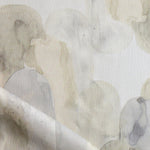 Detail of draped fabric in watercolor elongated pill pattern in soft beige and taupe on a white field.