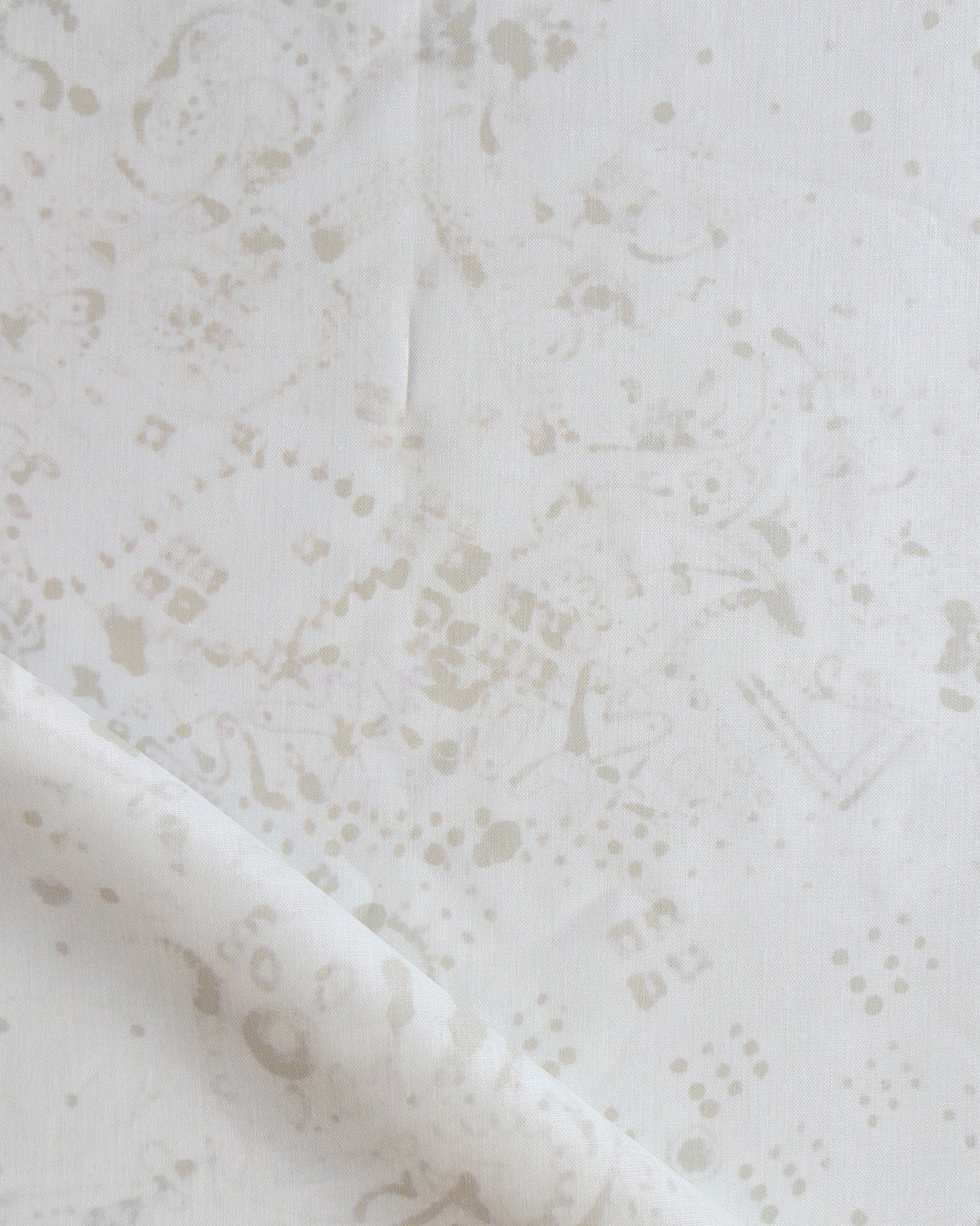 Detail of draped fabric in a painterly bandana print in beige on a cream field.