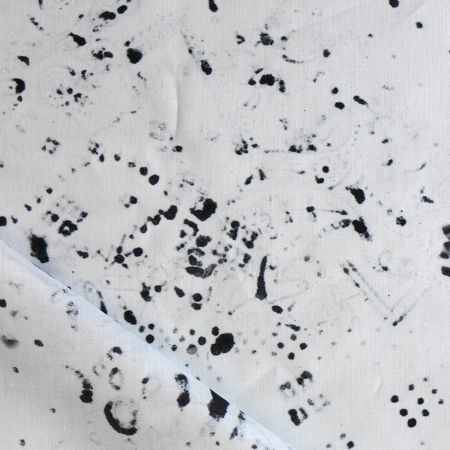 Detail of draped fabric in a painterly bandana print in black on a cream field.