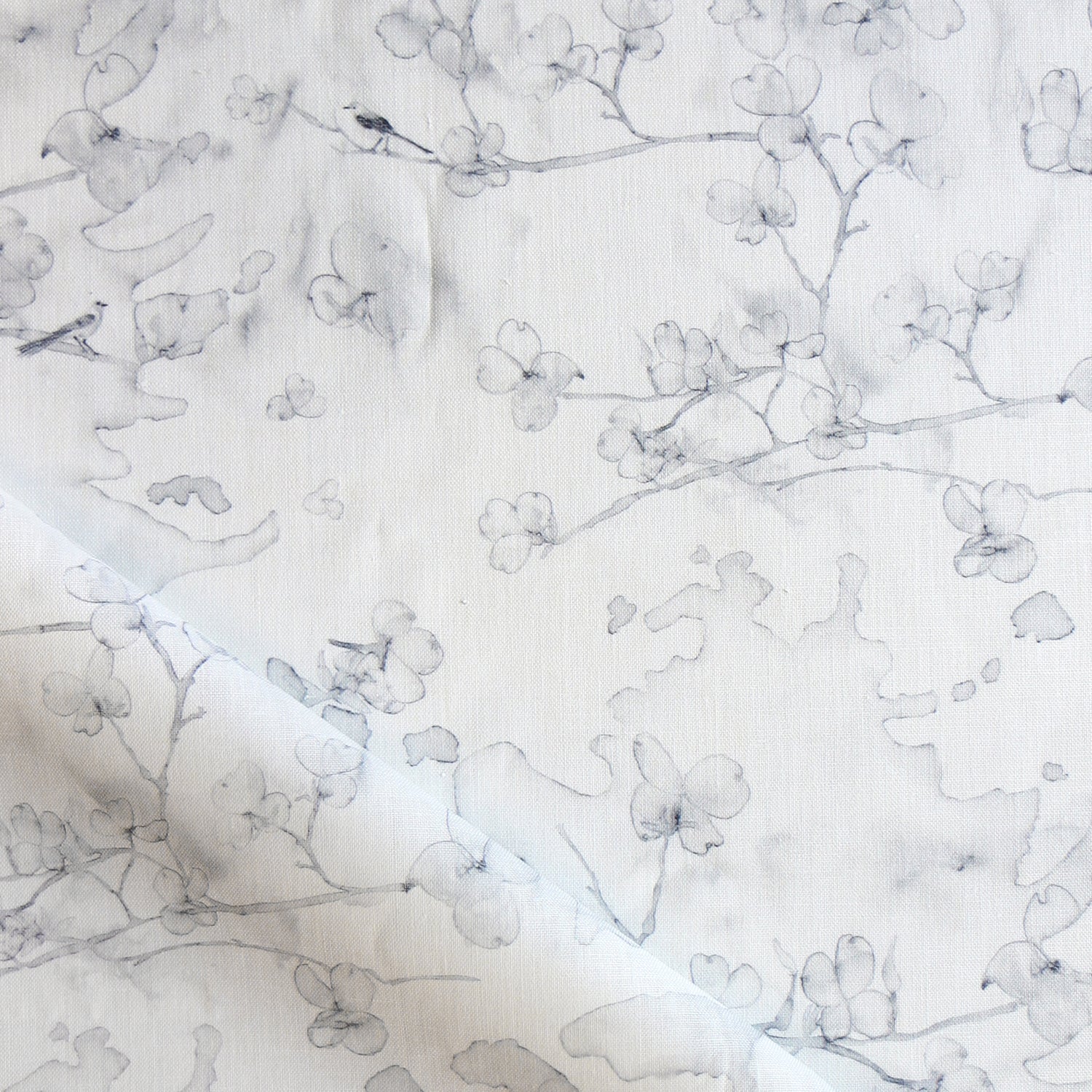 Draped fabric in a watercolor branch and floral pattern in soft grey on a white field