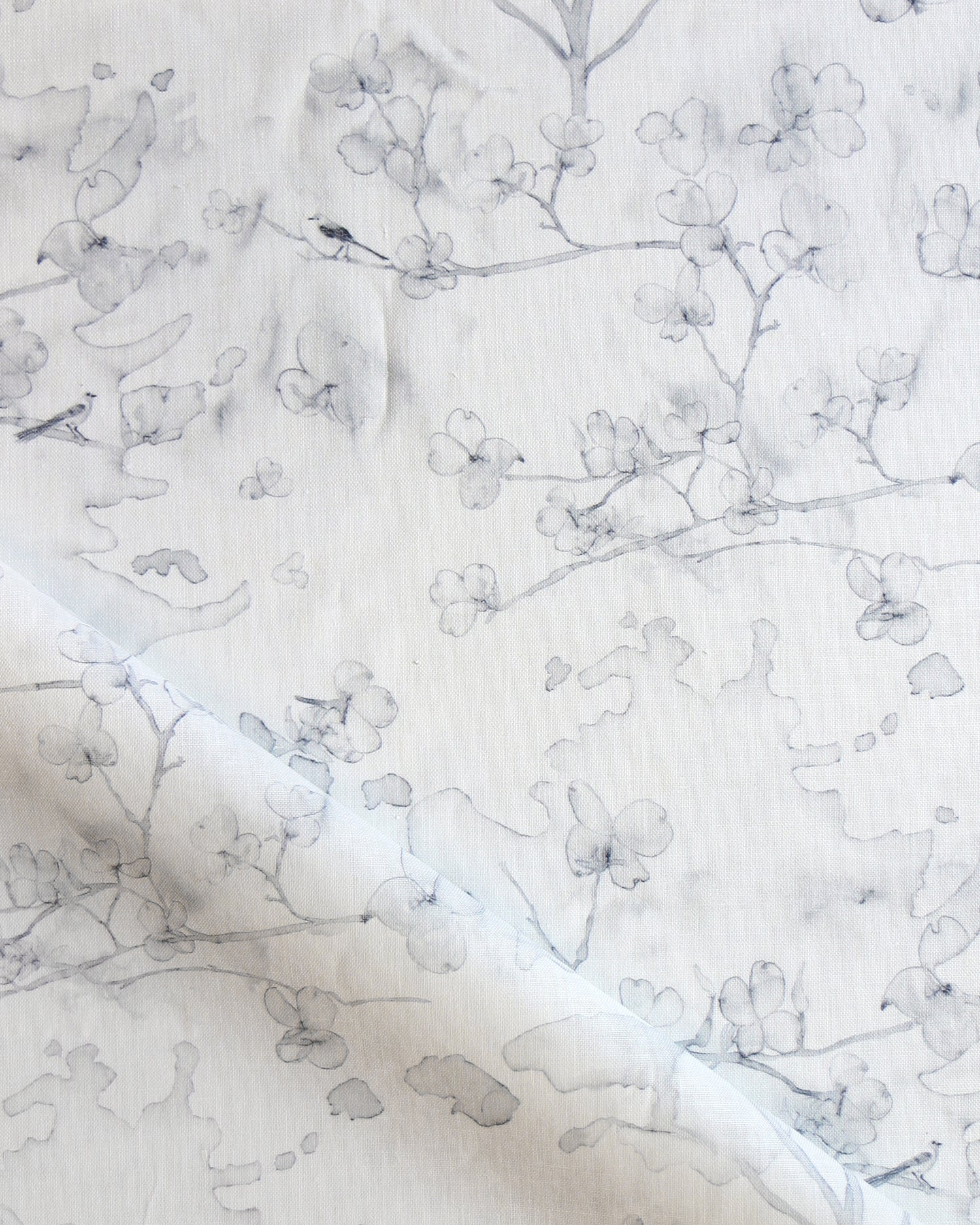Draped fabric in a watercolor branch and floral pattern in soft grey on a white field