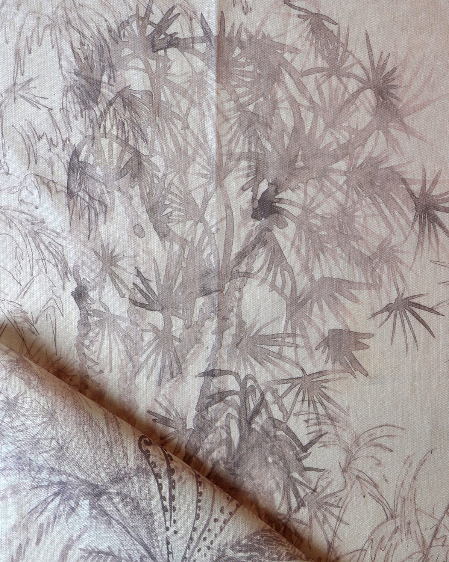 Detail of draped fabric in a painterly palm tree print in light pink on a cream field.