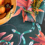 Detail of tablecloth vignette in a playful leaf and snake print in pink, blue and green on a dark turquoise field.