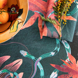 Detail of tablecloth vignette in a playful leaf and snake print in pink, blue and green on a dark turquoise field.