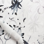 Detail of draped fabric in a playful leaf and snake print in gray and navy on a cream field.