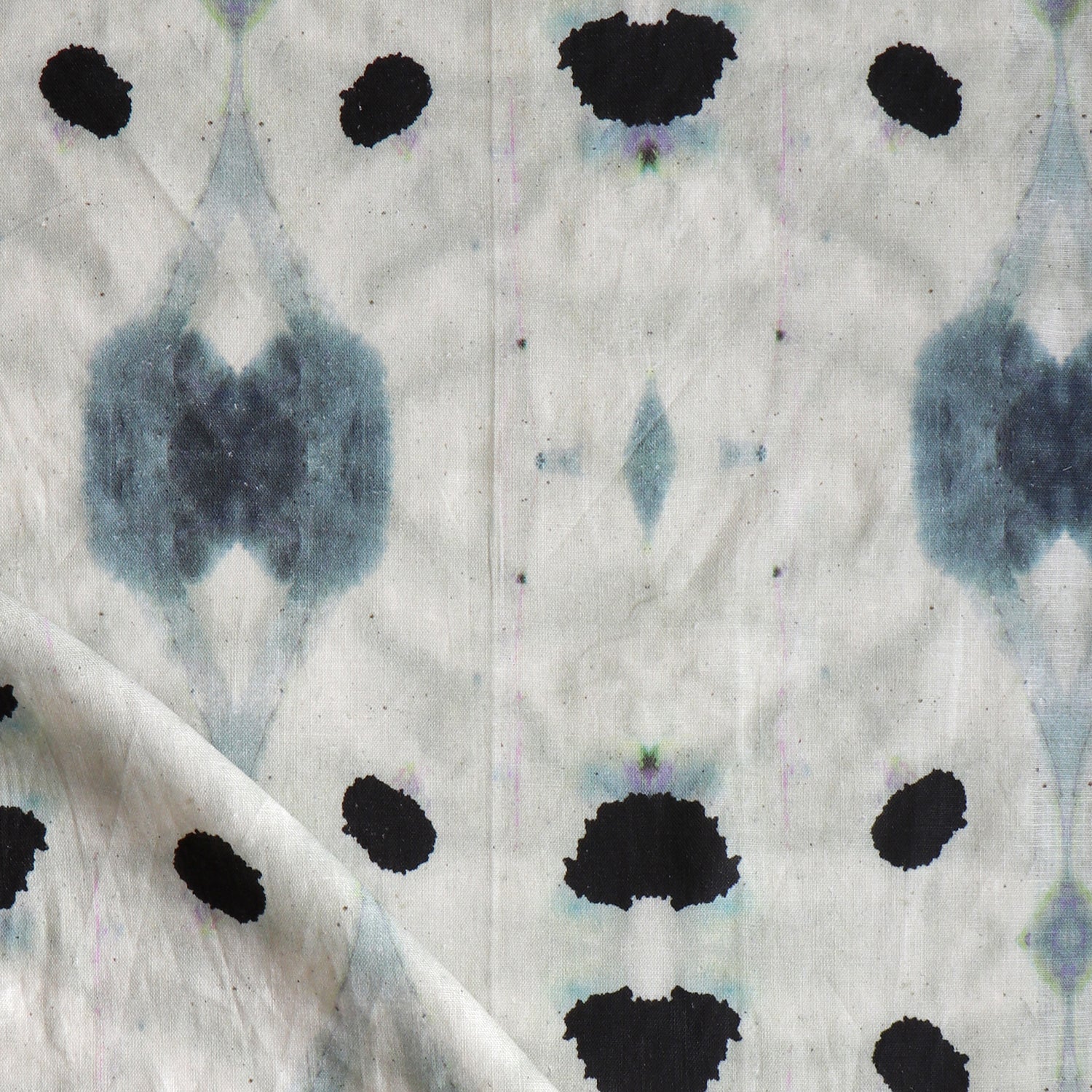 Detail of draped fabric in a watercolor ink blot print in shades of charcoal and black on a tan field.