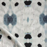 Detail of draped fabric in a watercolor ink blot print in shades of charcoal and black on a tan field.