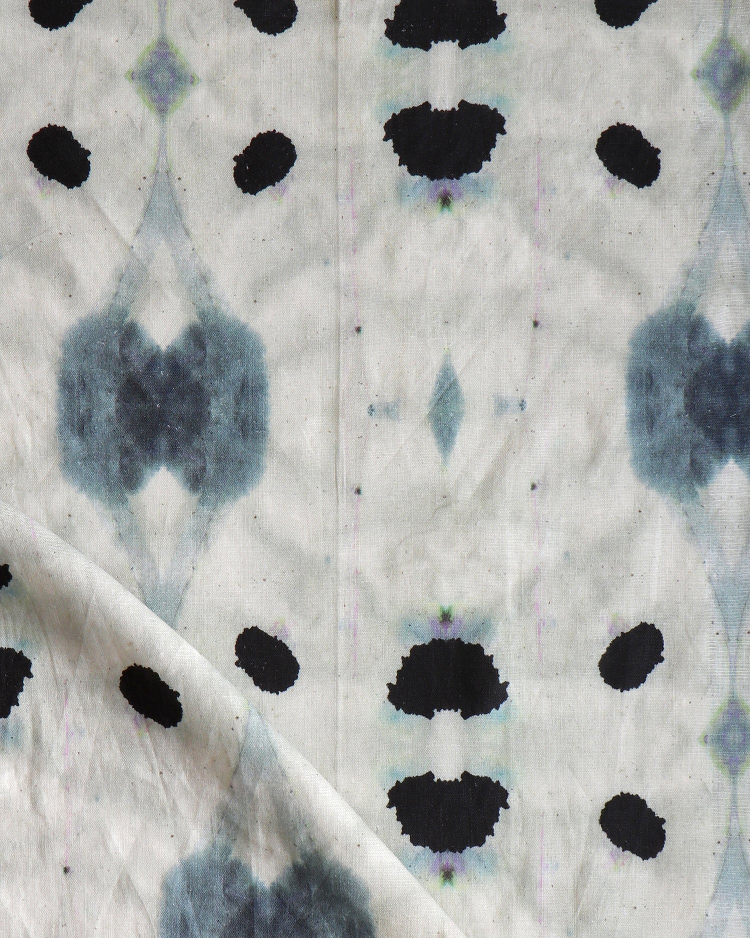 Detail of draped fabric in a watercolor ink blot print in shades of charcoal and black on a tan field.