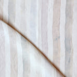 Detail of draped fabric in a painterly stripe print in shades of pink, gray and cream on a white field.