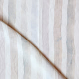 Detail of draped fabric in a painterly stripe print in shades of pink, gray and cream on a white field.