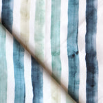 Detail of draped fabric in a painterly stripe print in shades of blue, green and tan on a white field.