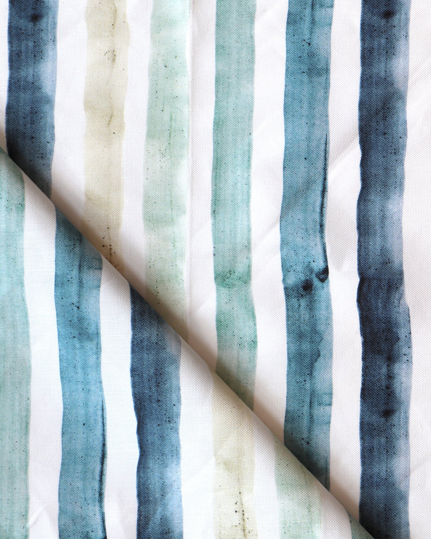Detail of draped fabric in a painterly stripe print in shades of blue, green and tan on a white field.
