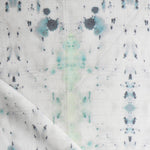 Detail of draped fabric in a watercolor ink blot print in gray and green on a cream field.