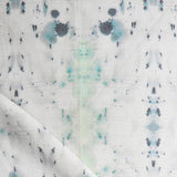 Detail of draped fabric in a watercolor ink blot print in gray and green on a cream field.