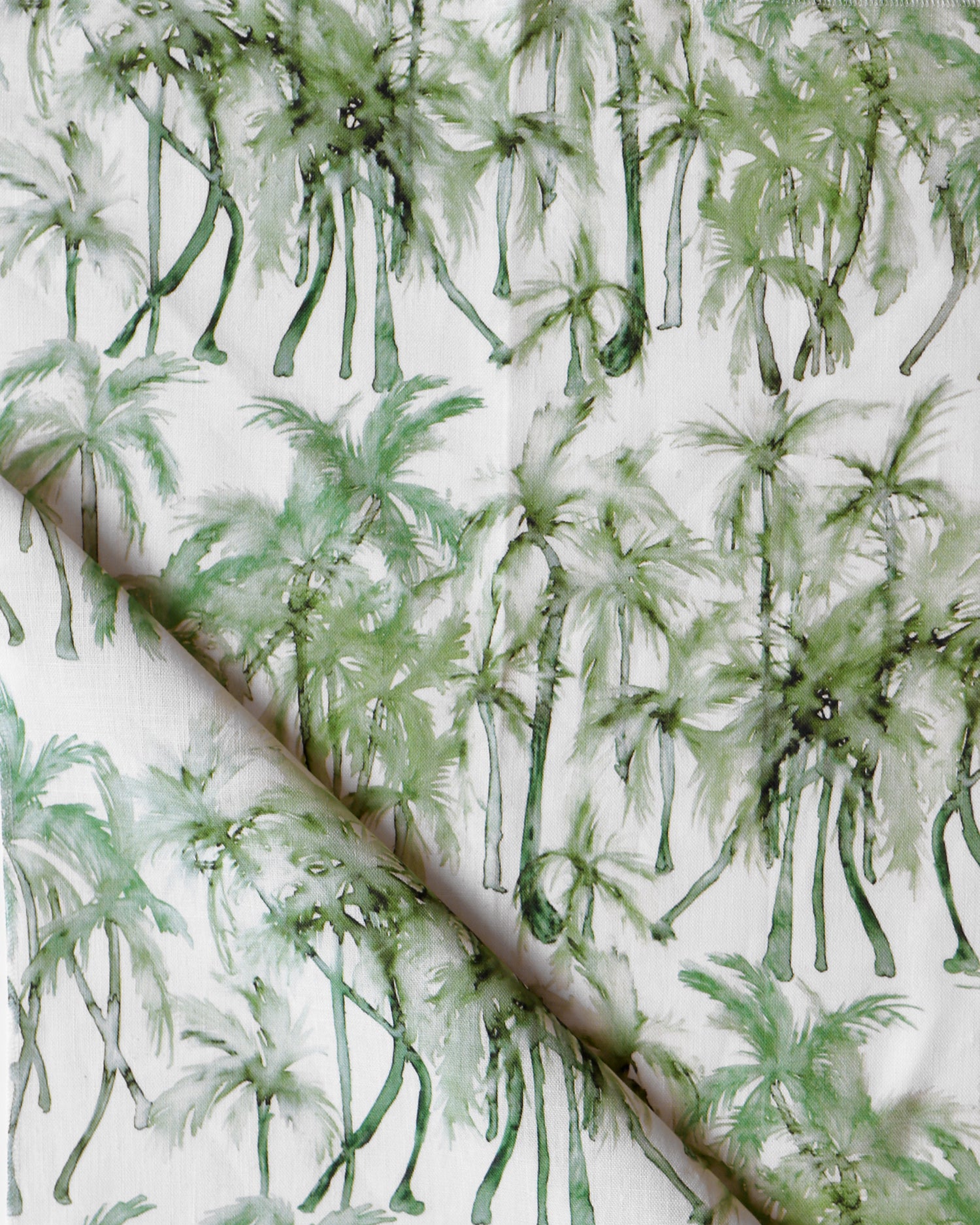 Detail of draped fabric in a painterly palm tree stripe print in shades of green on a white field.