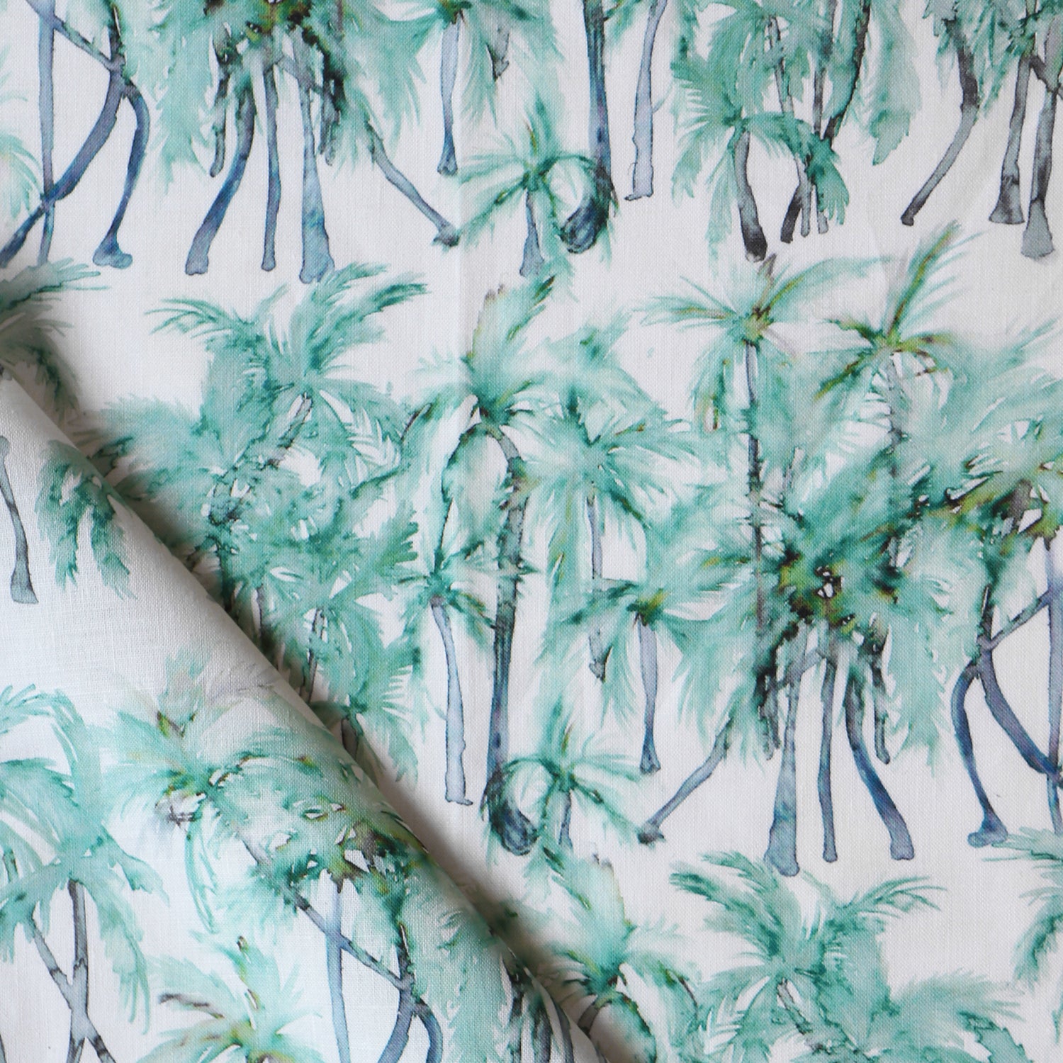 Detail of draped fabric in a painterly palm tree stripe print in shades of green and gray on a white field.