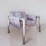 Chrome side chair upholstered with fabric in a painterly herringbone print in shades of blue, pink and orange.