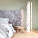 Bedroom vingette with upholstered headboard in a painterly palm tree pattern in shades of purple and navy on a gray field.