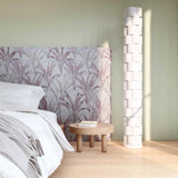 Bedroom vingette with upholstered headboard in a painterly palm tree pattern in shades of purple and navy on a gray field.