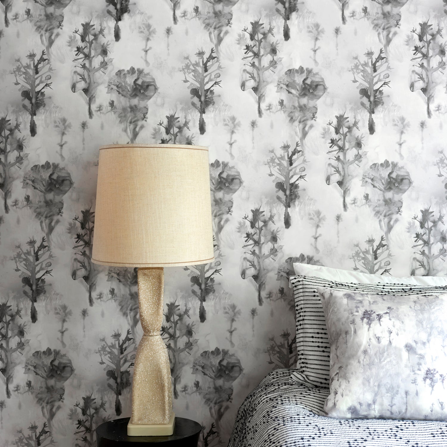 Bedroom scene against a watercolor tree print in shades of gray and black on a white field.