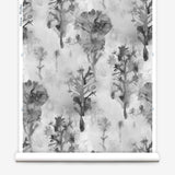 Wallpaper roll in a watercolor tree print in shades of gray and black on a white field.