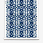 Wallpaper roll in a watercolor ikat stripe print in shades of white and blue on a gray field.