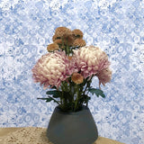 Bouquet of pink and brown flowers in a gray vase against a decorative blue and white patterned wall.