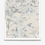 Wallpaper roll in a watercolor branch and floral pattern in grey and blue on a taupe muted taupe field. 