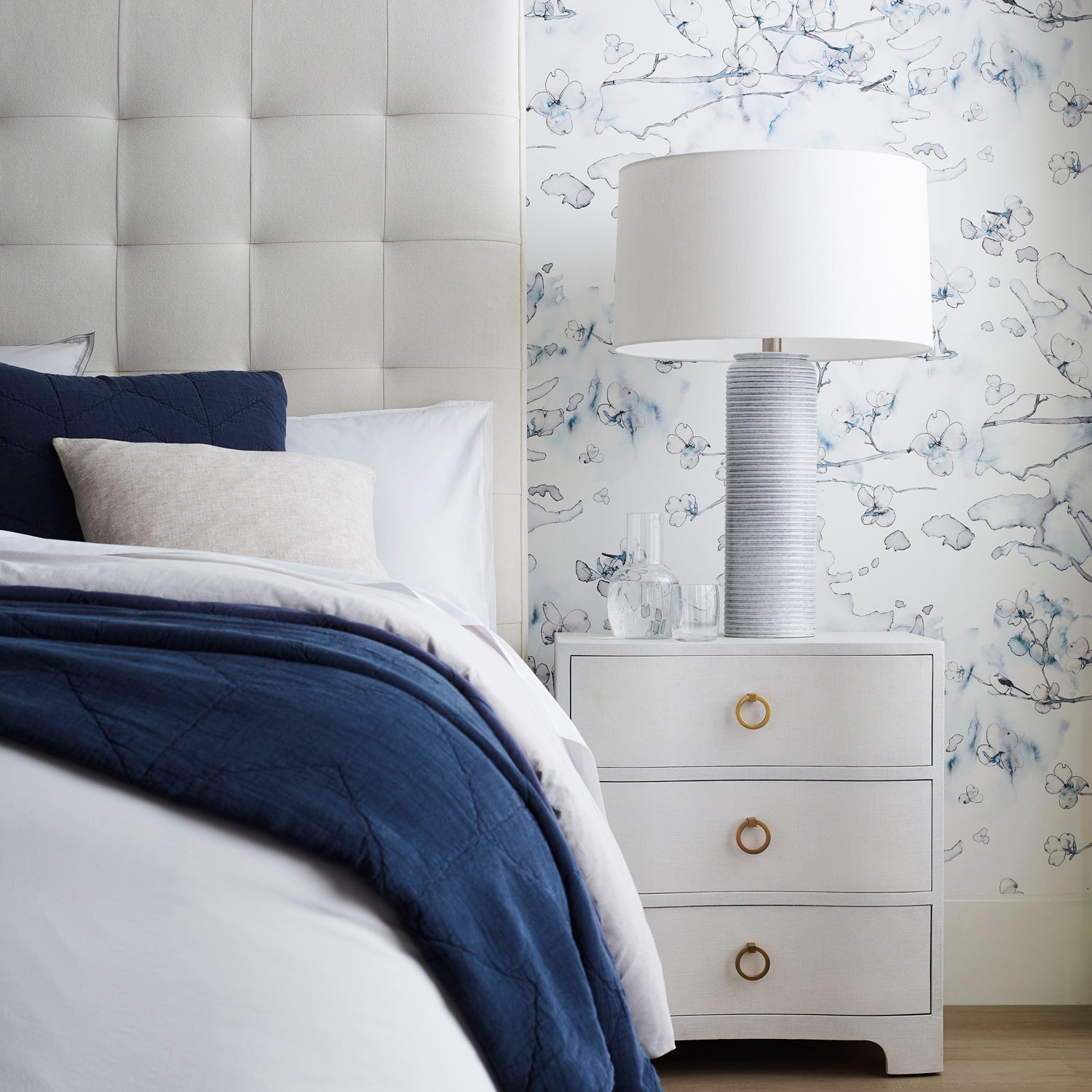 Preppy white bedroom scene against wallpaper in watercolor branch and floral pattern in shades of blue on a white field.