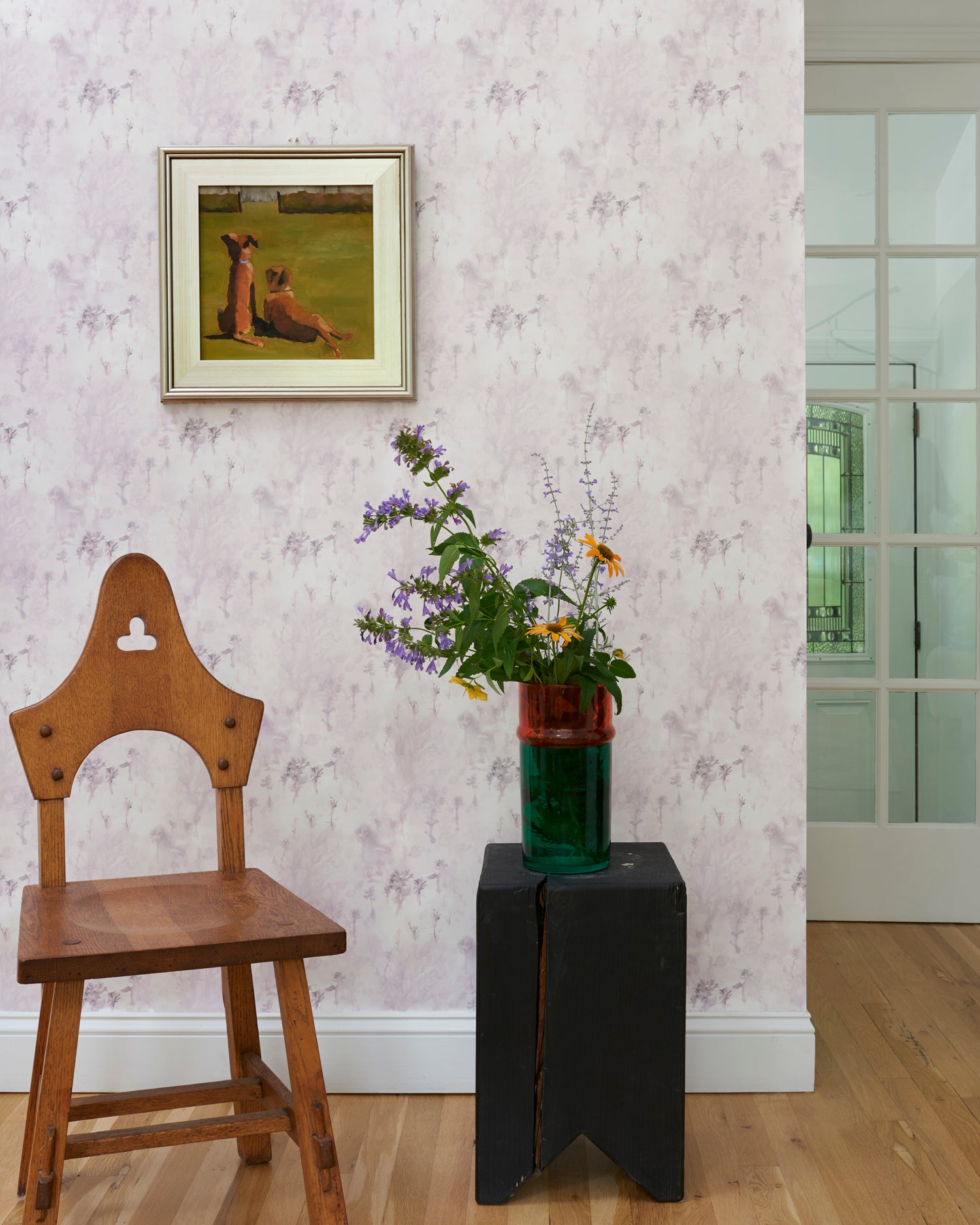 Wallpaper light purple painterly tree pattern framed by wooden chair, side table with flowers and an oil painting. 