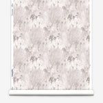 Wallpaper roll in a painterly tree print in light pink and purple on a cream field.