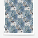 Wallpaper roll in a painterly tree print in blue, gray and tan on a white field.