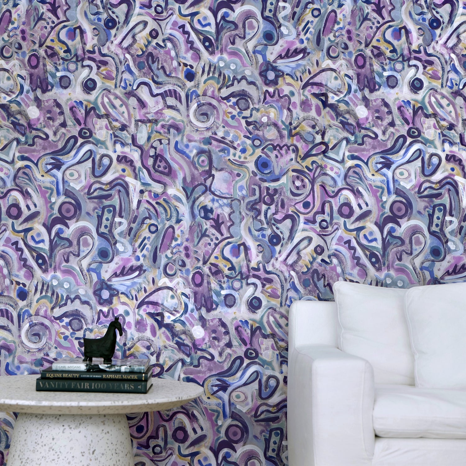 White couch and marble side table against wallpaper in abstract brushstroke design in shades of purple and black accents. 