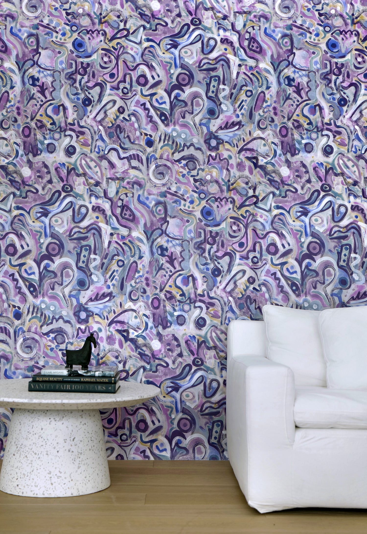 White couch and marble side table against wallpaper in abstract brushstroke design in shades of purple and black accents. 
