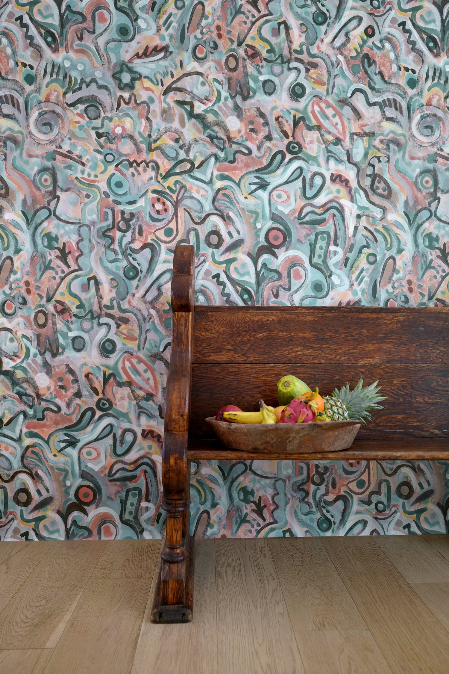 Wooden bench against wallpaper in abstract brushstroke design in shades of teal, rust brown and black accents. 