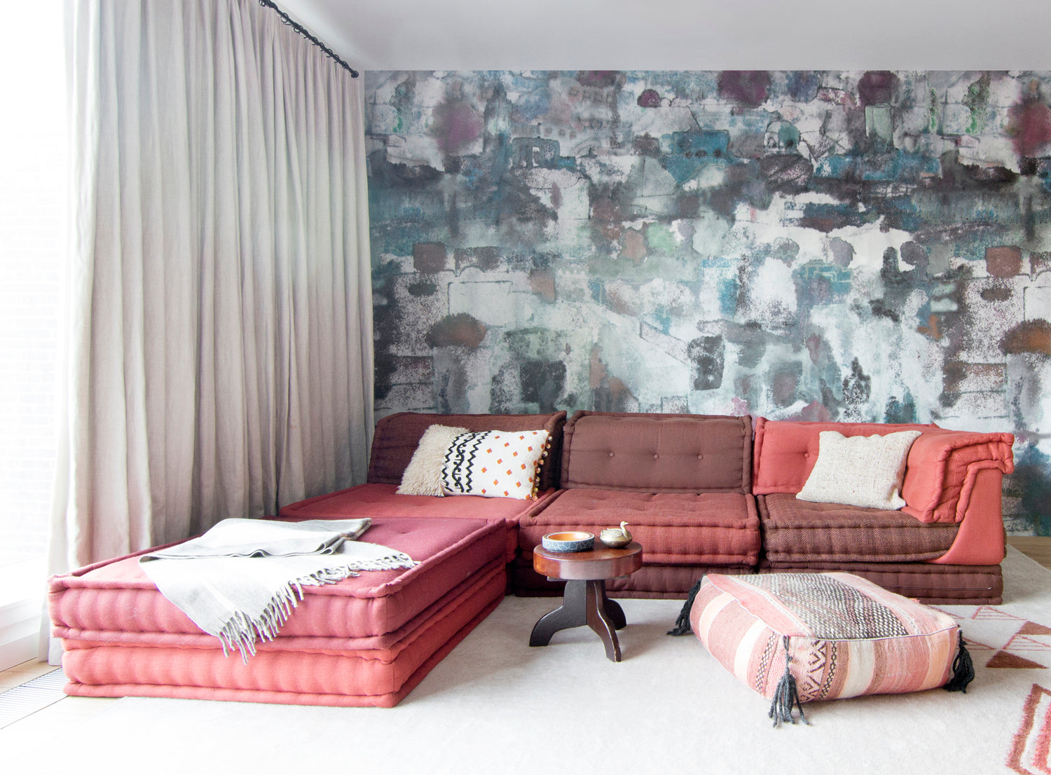 Living room scene with red bohemian couch with a paint splatter wallpaper mural in green, brown and pink.