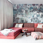 Living room scene with red bohemian couch with a paint splatter wallpaper mural in green, brown and pink.