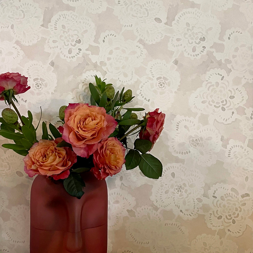 Vase shaped like a face with flowers on top of books against a patterned wall.