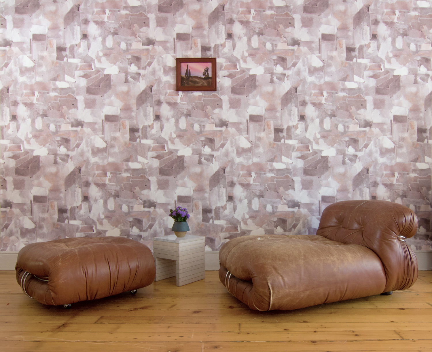 Modern camel leather accent chair against wallpaper in a textural paint blotch print in shades of brown and tan on a white field.