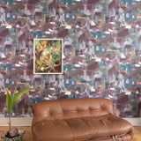 Modern camel leather couch against wallpaper in a textural paint blotch print in shades of purple, turquoise and green on a gray field.