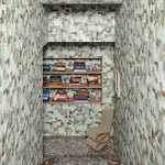 Stone staircase down to a landing with chair and built in book case surrounded by green abstract puzzle wallpaper. 
