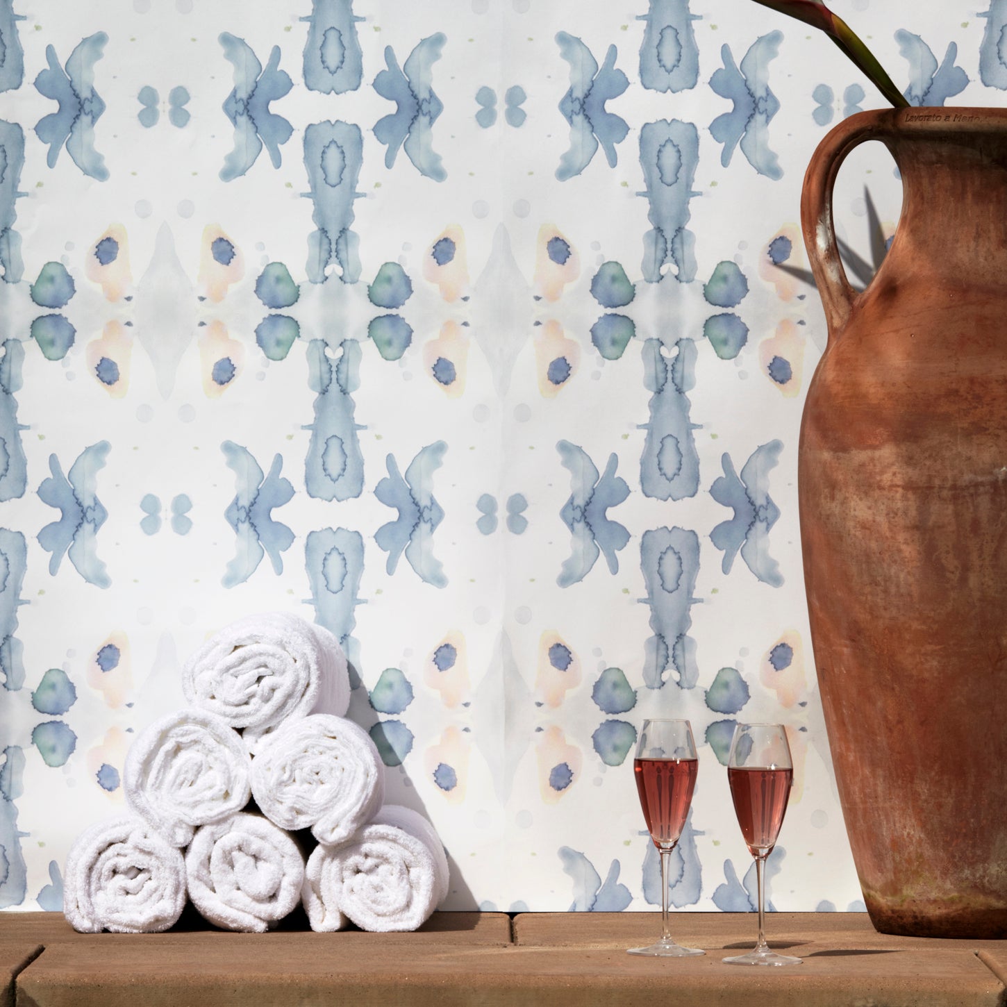 Wallpaper installed behind a plunge pool with props in a watercolor ink splash print in shades of pastel blue and pink on a cream field.